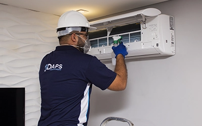 Técnico da DAPS Climatização realizando limpeza e higienização de ar-condicionado split de parede em Campinas, utilizando equipamentos de proteção.
