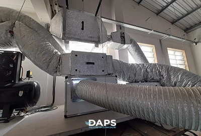 Sistema de dutos de ar-condicionado industrial em galpão, com caixas de insuflação e retorno conectadas por dutos flexíveis e metálicos instalados pela DAPS Climatização.