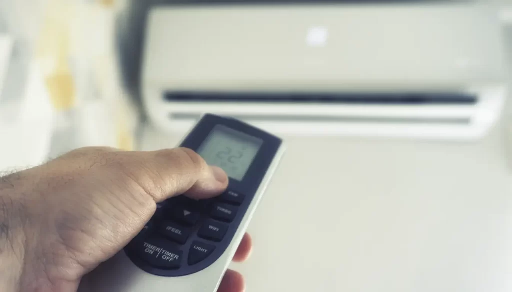Mão segurando controle remoto apontado para ar-condicionado split ajustado para 22 graus.