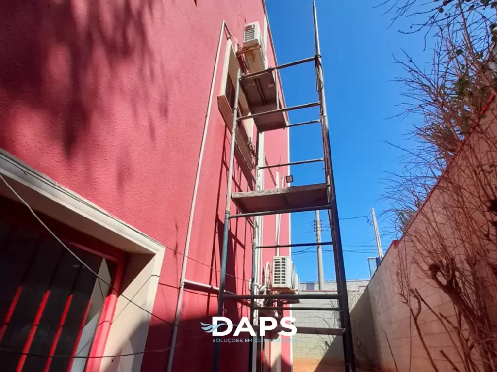 Edifício residencial com fachada rosa mostrando múltiplas unidades externas de ar-condicionado instaladas em estrutura metálica, demonstrando instalação em larga escala de sistemas de climatização.