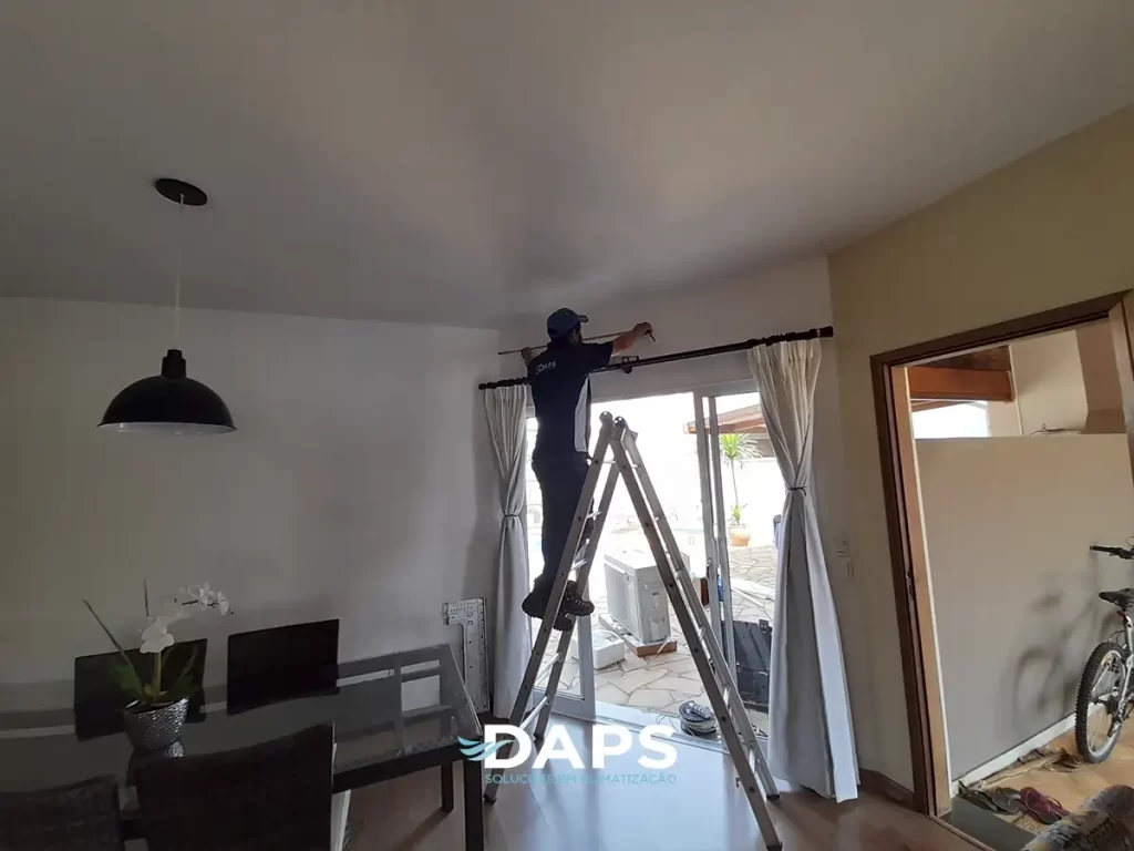 Técnico da DAPS realizando instalação de ar-condicionado tipo split inverter em ambiente residencial, posicionando a unidade interna na parede com auxílio de escada, demonstrando instalação profissional.