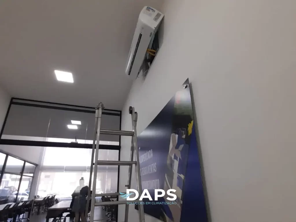 Técnico instalando unidade interna de ar-condicionado em parede de escritório em Campinas, utilizando escada, ambiente com vidraçaria e iluminação LED, demonstrando processo de climatização profissional.
