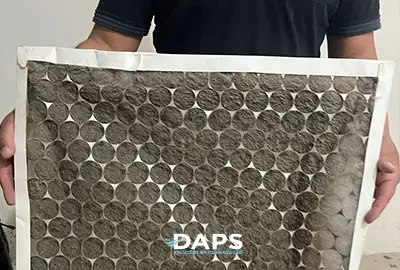 Filtro de ar de climatizador evaporativo DAPS muito sujo, com acúmulo de poeira, sendo segurado para inspeção em Campinas