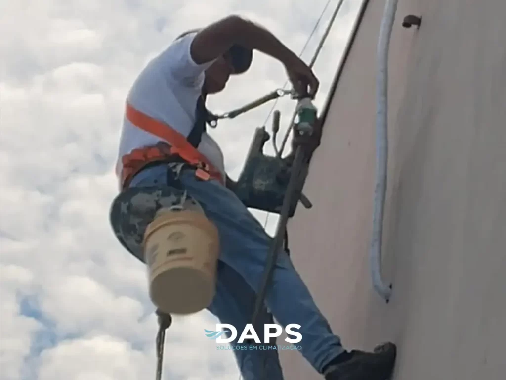 Técnico prestador de serviço escalando parede externa de edifício com equipamento de segurança, realizando manutenção ou instalação de ar-condicionado em fachada de igreja em Campinas.