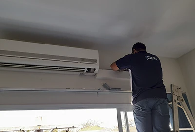 Técnico profissional DAPS instalando unidade evaporadora de ar condicionado split em teto de sala comercial no Centro de Campinas, com equipamento de segurança e precisão técnica. Campinas Ar Condicionado.